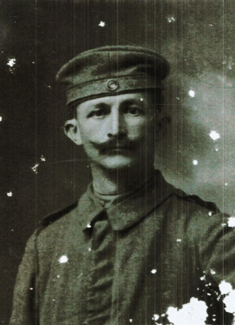 Porträt eines Mannes mit Schnurrbart in Uniformjacke und Feldmütze; das Bild hat helle Flecken.