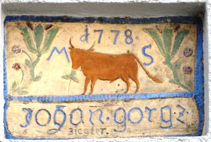 Farbig bemaltes Hauszeichen mit einem braunen Rind zwischen Blumen, den Buchstaben M und S, der Jahreszahl 1778 und der Inschrift „Johan Gorg Z“.
