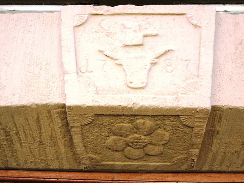 Hell gestrichener Schlussstein mit einem Rinderkopf, Initialen und der Jahreszahl 1787, darunter eine Rosette.