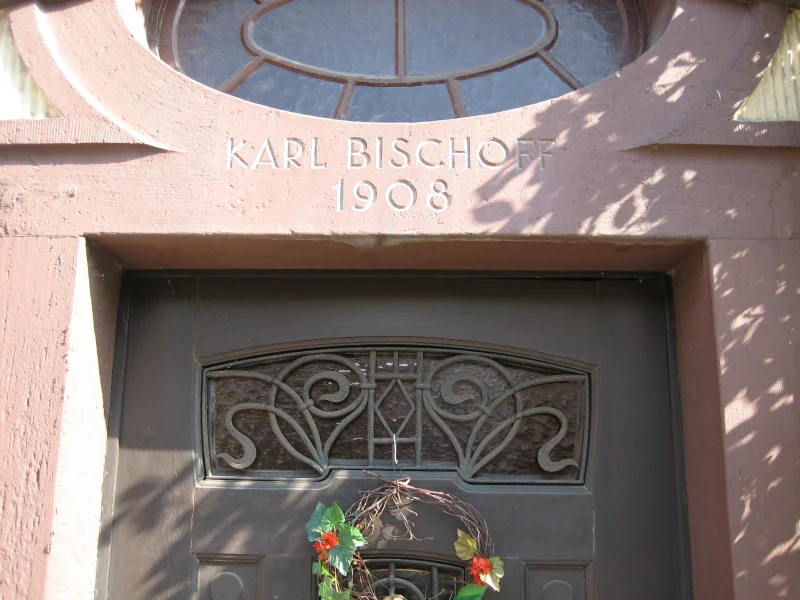 Über einer Haustür mit Jugendstilgitter steht die Inschrift „Karl Bischoff 1908“.